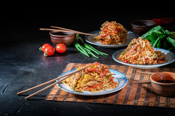 Udon noodles with fried chicken, shrimps (prawns) and vegetables on dark background