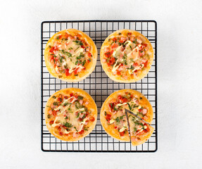 Mini pizzas with sausage, pickles, tomatoes, mozzarella, greens on a metal stand on a white background top view 