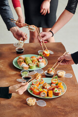 Obraz na płótnie Canvas Sushi set on table in office. Party of friends eating sushi rolls using bamboo sticks. Corporate