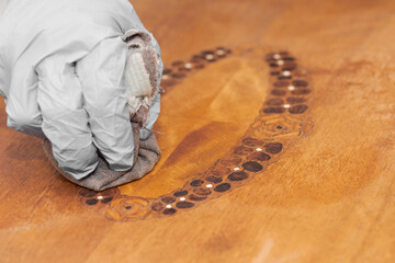 Human hand with rubber gloves polishing shellac with pumice into wood of old furniture for...