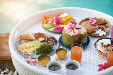 Many of natural and healthy asian food fruits and drinks on white floating table around swimming pool in daytime.