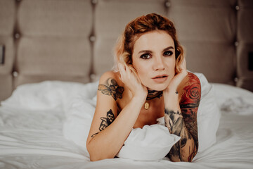 Portrait of a happy beautiful girl with tattoos. The woman is lying in bed.