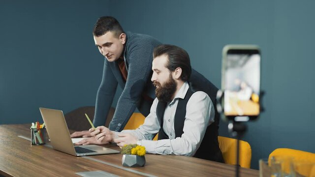 Broadcast a meeting of two young people discussing a business strategy while working with a notebook. Capture a conference on a mobile phone.