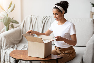 Happy young woman unpacking delivery box, home interior - obrazy, fototapety, plakaty