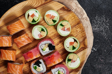 Fototapeta na wymiar Sushi set with Philadelphia, roll with avocado and roll with tuna on round wooden board on dark background. Close-up. Top view 