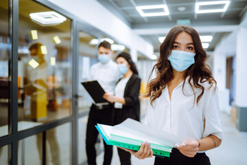 Portrait of young business woman in protective face mask an office building hallway. Office worker working during pandemic in quarantine city. COVID - 19.