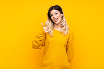 Teenager girl isolated on yellow background showing ok sign and thumb up gesture