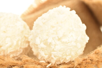 Two round candies with coconut flakes on a jute napkin, close-up, isolated on white.