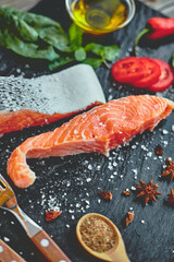 Raw salmon fillet and ingredients for cooking on a dark background.