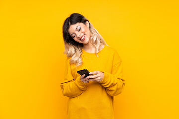 Teenager girl isolated on yellow background sending a message with the mobile