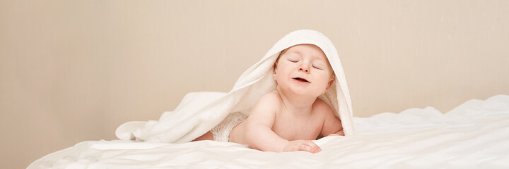 Fototapeta na wymiar Cute small boy lying at bed. Childhood bath concept. Light background. Little child. Serious calm emotion. Copyspace. Stay home. Towel mockup. Closed eyes. Horizontal banner