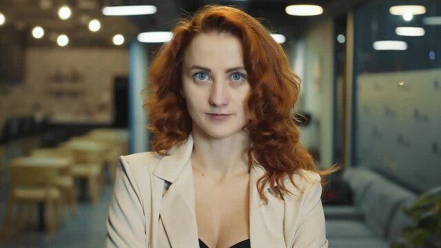 Face of a woman of European appearance with red hair close up. A woman with big blue eyes is forced to look at the camera. Focused young woman entrepreneur or manager.