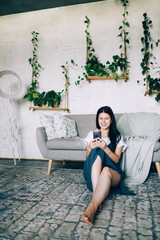Obraz premium The girl sits near the sofa and looks at the phone.
