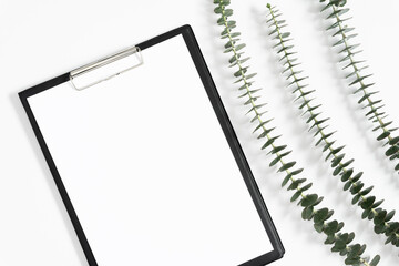 Black clipboard mockup with eucalyptus on white background. Flat lay, top view, copy space