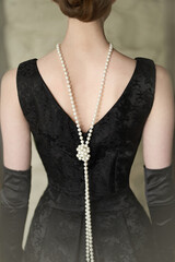 Beautiful female figure from the back in a black dress and pearls in the style of 20-30 years of the XX century