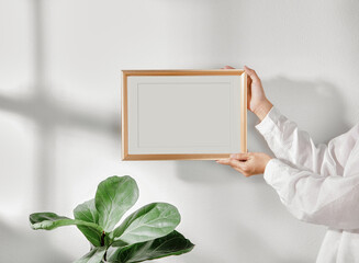 Hand holding Frame or Poster mock up in living room and window shadow on white wall background.