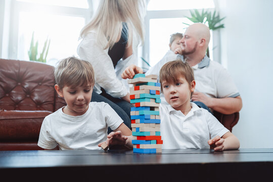 Weekend of happy caucasian family in modern apartment. Two little boys play jenga game competing who is better.