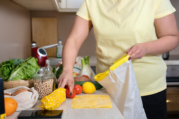 Unrecognisable woman in yellow T-shirt placing vegetables in eco friendly cotton bag. Zero waste and sustainable lifestyle