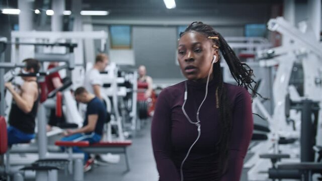 A black woman listening music and warming up in the gym - squatting