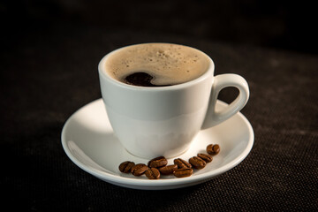 White cup of coffee on a saucer with coffee beans and marshmallows. Espresso. Close-up.
