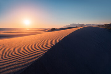 Atmospheric and mystical moody light of the sunset sunbeam illuminated the slope of a sand dune somewhere in the depths of the Sahara Desert - obrazy, fototapety, plakaty