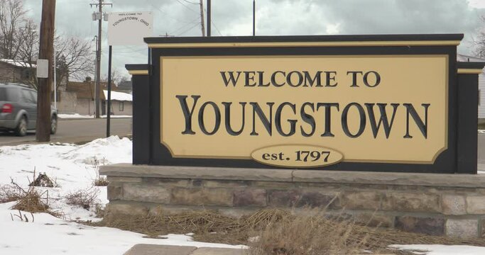 A closeup view of the Welcome to Youngstown sign as traffic passes by on a winter overcast day.
