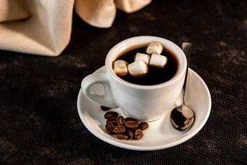 White cup of coffee on a saucer with coffee beans and marshmallows. Espresso. Close-up.