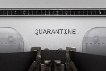 Typing text QUARANTINE on vintage manual typewriter. Close up of writes word on white paper. Shot in macro. Concept of Coronavirus COVID-19.