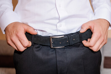 The groom tightens his belt. A man holding his hands on his belt