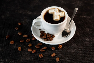 White cup of coffee on a saucer with coffee beans and marshmallows. Espresso. Close-up.