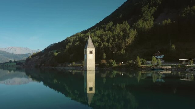 Amazing areal view of an old bell tower of Curon (Graun) the village rising out of the water Lake Resia on a beautiful morning with a blue sky.