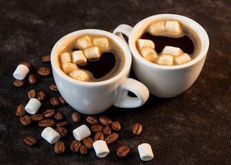 Two cups of coffee on a saucer with marshmallows and coffee beans on a dark background. Close-up.