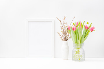Home interior with easter decor. Mockup with a white frame and pink tulips in a vase on a light background