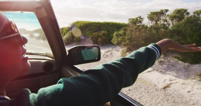 Mixed race woman driving on sunny day in convertible car waving arm and smiling - Powered by Adobe