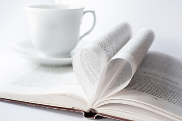 Open book with heart shape page and white coffee or tea cup. Love reading books concept. Romantic written love story.