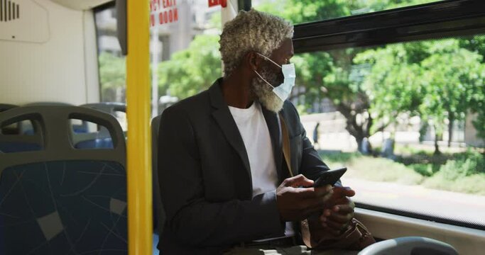 African american senior man wearing face mask using smartphone while sitting in the bus