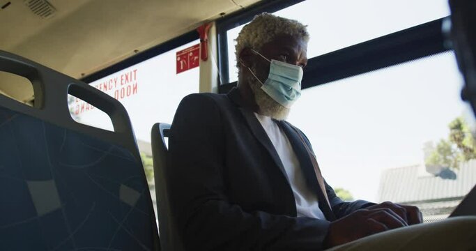 African american senior man wearing face mask using laptop while sitting in the bus