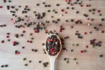 Wooden spoon with different kinds sort of peppercorns on wooden background. Top view. Copy space.