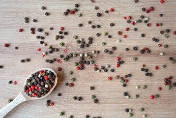 Wooden spoon with different kinds sort of peppercorns on wooden background. Top view. Copy space.
