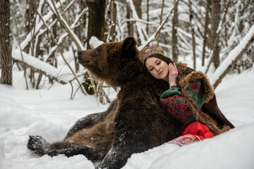  beautiful russian girl in national costume with a brown bear in the winter forest