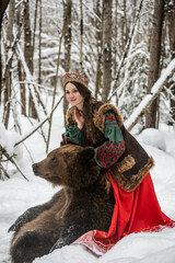  beautiful russian girl in national costume with a brown bear in the winter forest