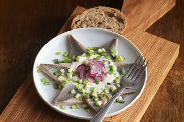 Herrings fillets with cream sauce with cucumbers, red onion and spices on cutting wooden board