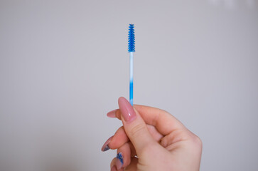 Hand holding a brush for eyelashes and eyebrows. Blue, white brush in master's hand. Professional beauty makeup tools for eyelashes and eyebrows.