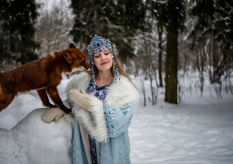 beautiful russian girl in national costume with a red fox in the winter forest