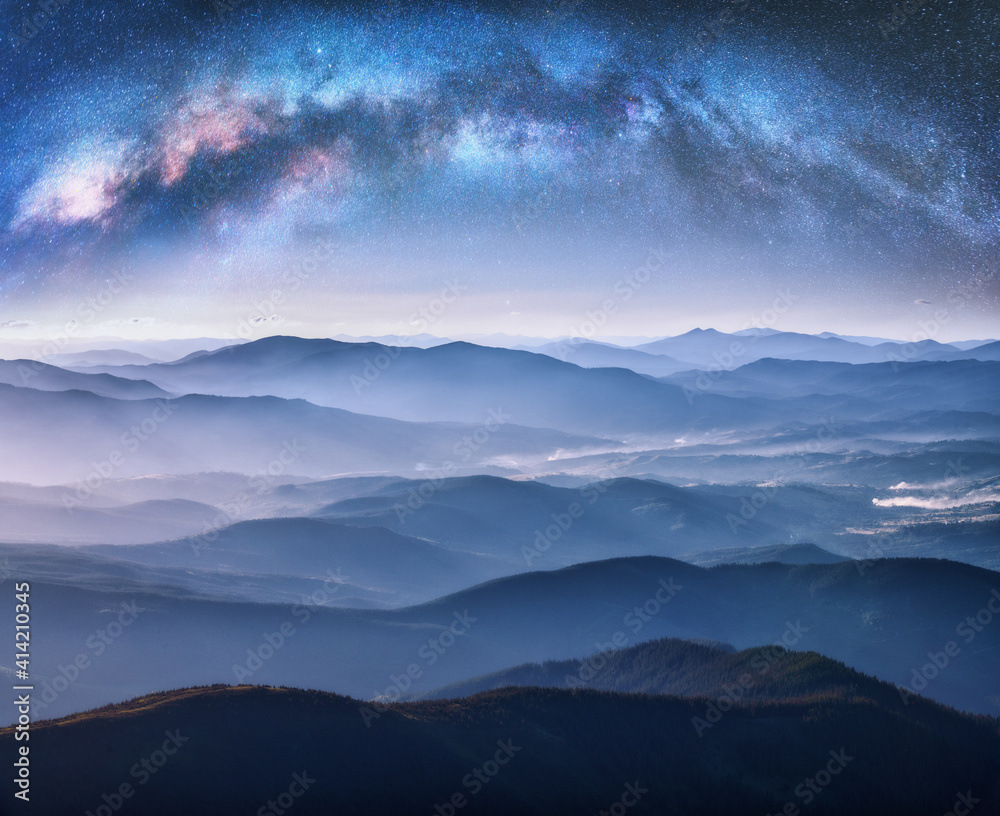 Wall mural milky way arch over the mountains in fog at starry night in summer. landscape with blue sky with sta