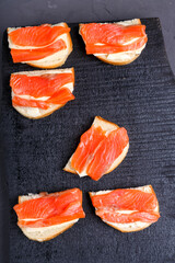 Bruschettes with butter and red fish on a black wooden board.