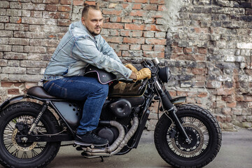 Obraz na płótnie Canvas Brave brutal casual motorcycle driver. Snarling beast bike with a black helmet against a brick wall. Outdoor portrait