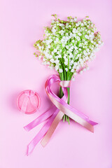 a bouquet of lily of the valley flowers with pink ribbons and a pink box with jewelry on a pink background close-up