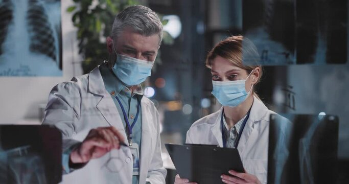 Caucasian professional couple of doctor microbiologist and female physician dicsovering symptoms of coronavirus disease looking on lung x-ray pictures in hospital office.