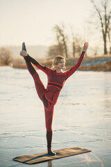 Fototapeta na wymiar A girl does yoga in winter on the ice of the lake during the sunset